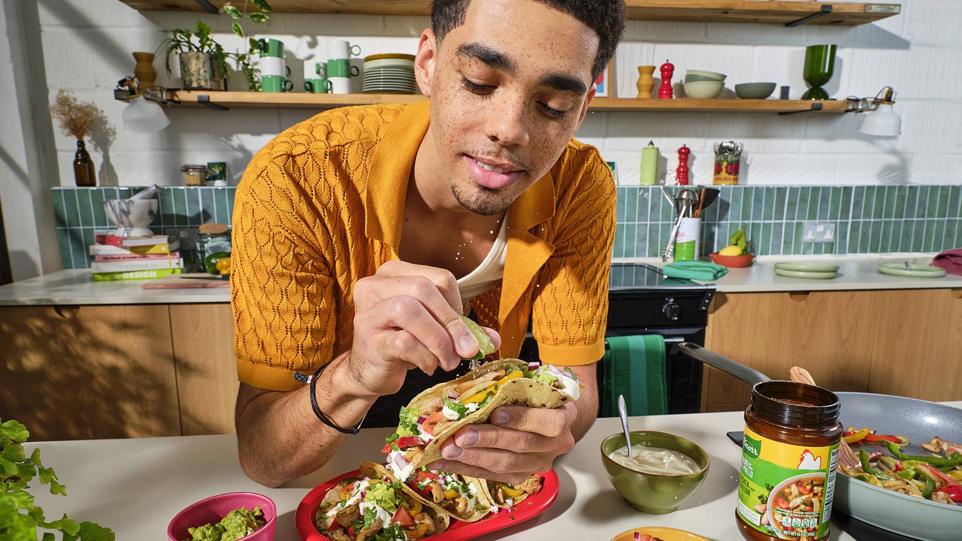 Man met een burrito in zijn hand in de keuken. Hij glimlacht. Hij sprenkelt wat limoensap over de burrito.