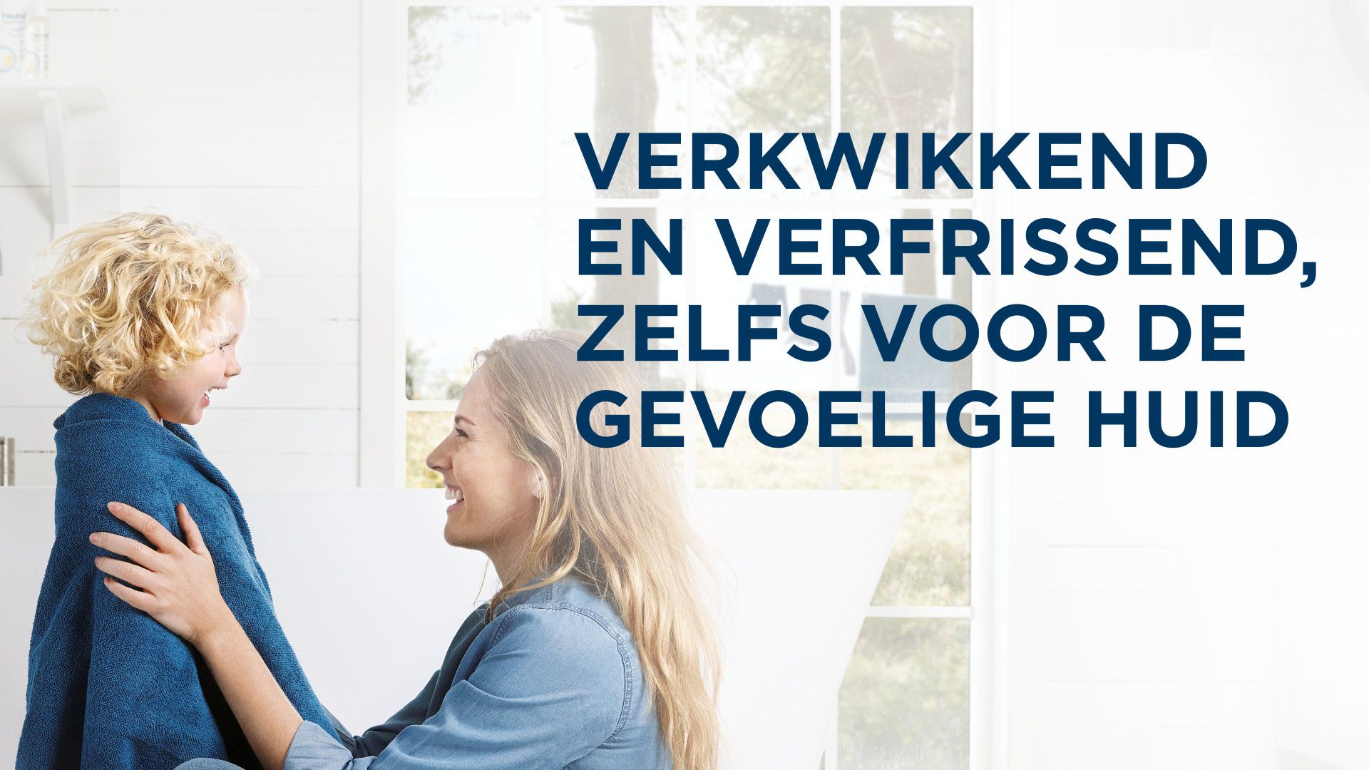 Een vrouw heeft een vriendelijke interactie met een kind dat in een blauwe handdoek is gewikkeld, in een lichte en luchtige badkamer.