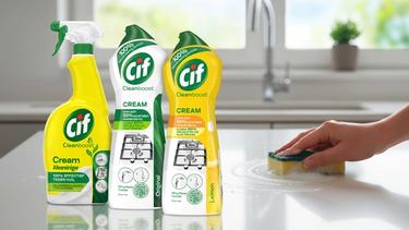 Drie flessen van Cif op het keukenblad. en een hand van iemand die met een sponsje poetst.