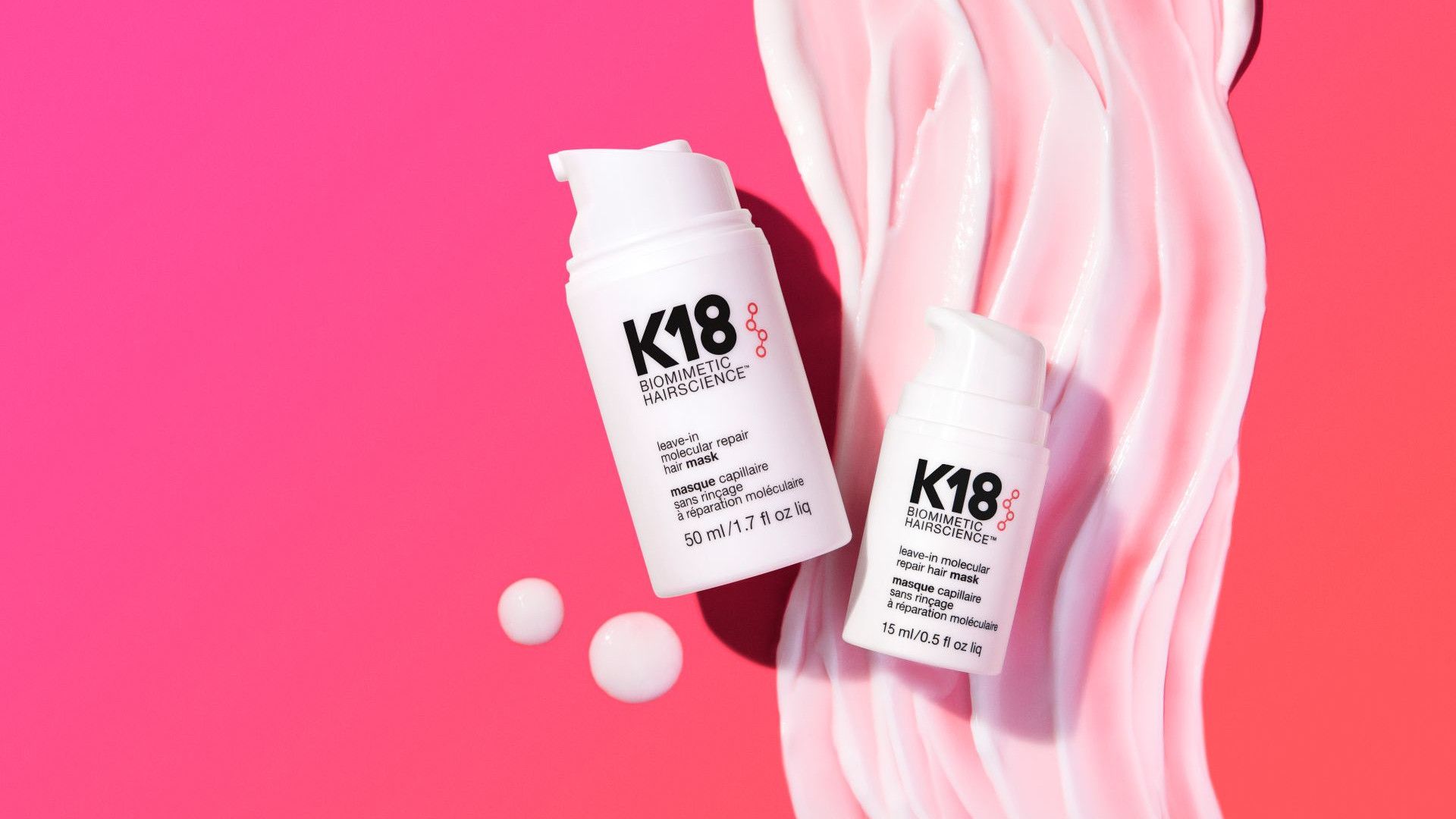 Twee witte flessen K18-haarbehandeling op een roze achtergrond met golvende crème.