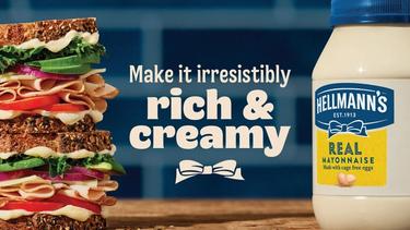 Op de banner staat een grote sandwich belegd met tomaat, kipfilet, komkommer, uit en sla. rechts daarvan een grote pot Hellman's mayonaise. in het midden staat de quote “make it irresistibly. rich & creamy”