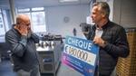 Op links Johan de Boterhammenman vol ongeloof kijkend naar cheque van €180.000 geschonken door Unilever.